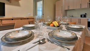 Un'area pranzo con un tavolo apparecchiato per due persone, con piatti a motivi floreali, bicchieri da vino e una ciotola di frutta.