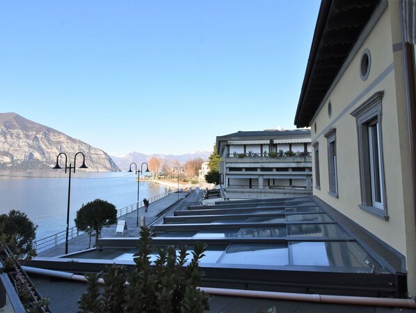 Un edificio con terraza que da a un cuerpo de agua, con montañas al fondo.