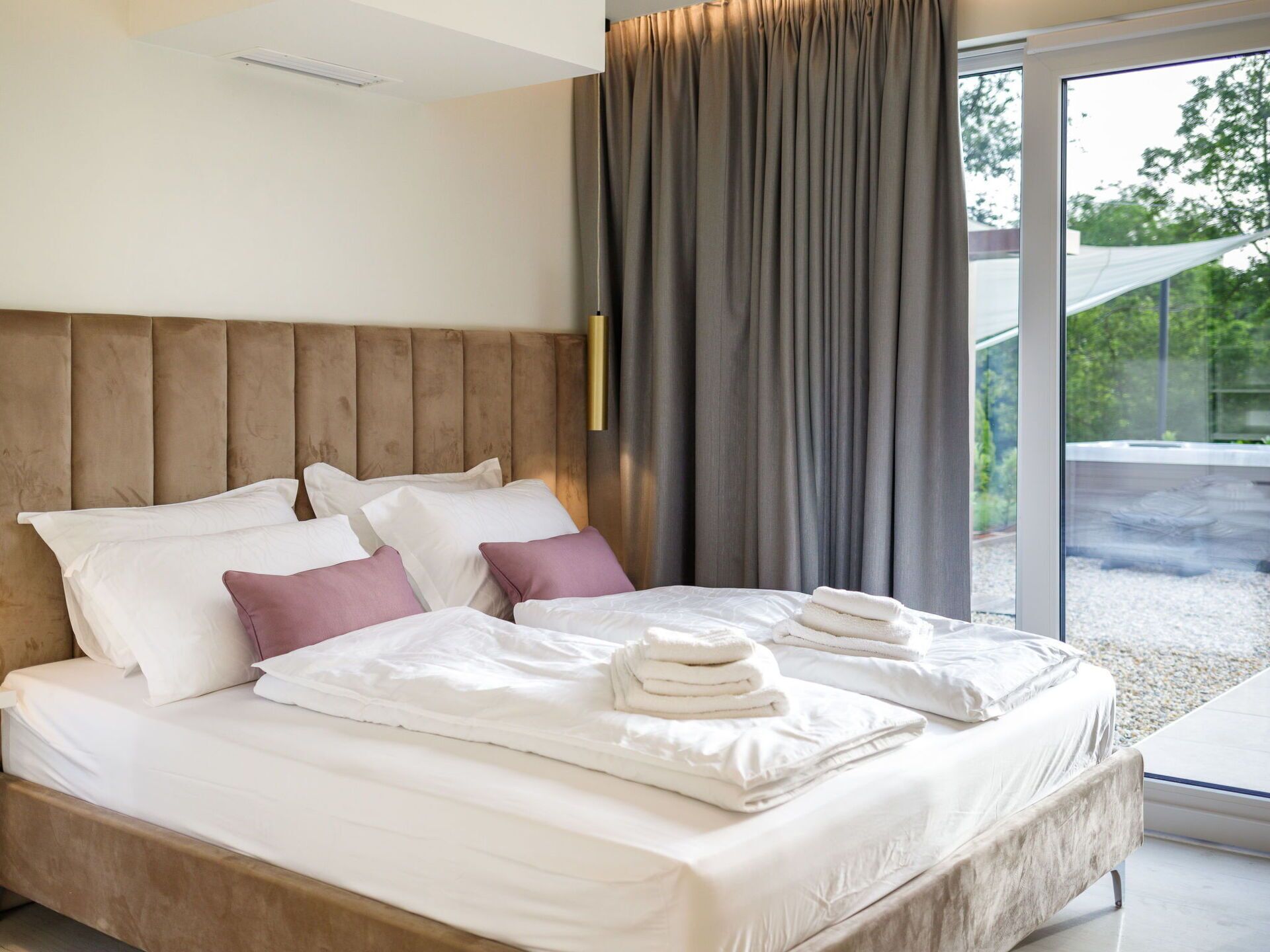 Une chambre moderne avec un grand lit, une tête de lit en bois et une vue sur un jardin, accessible par une porte-fenêtre coulissante.