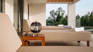 A modern outdoor lounge area with a sofa, a wooden table with candles, and a view of greenery.
