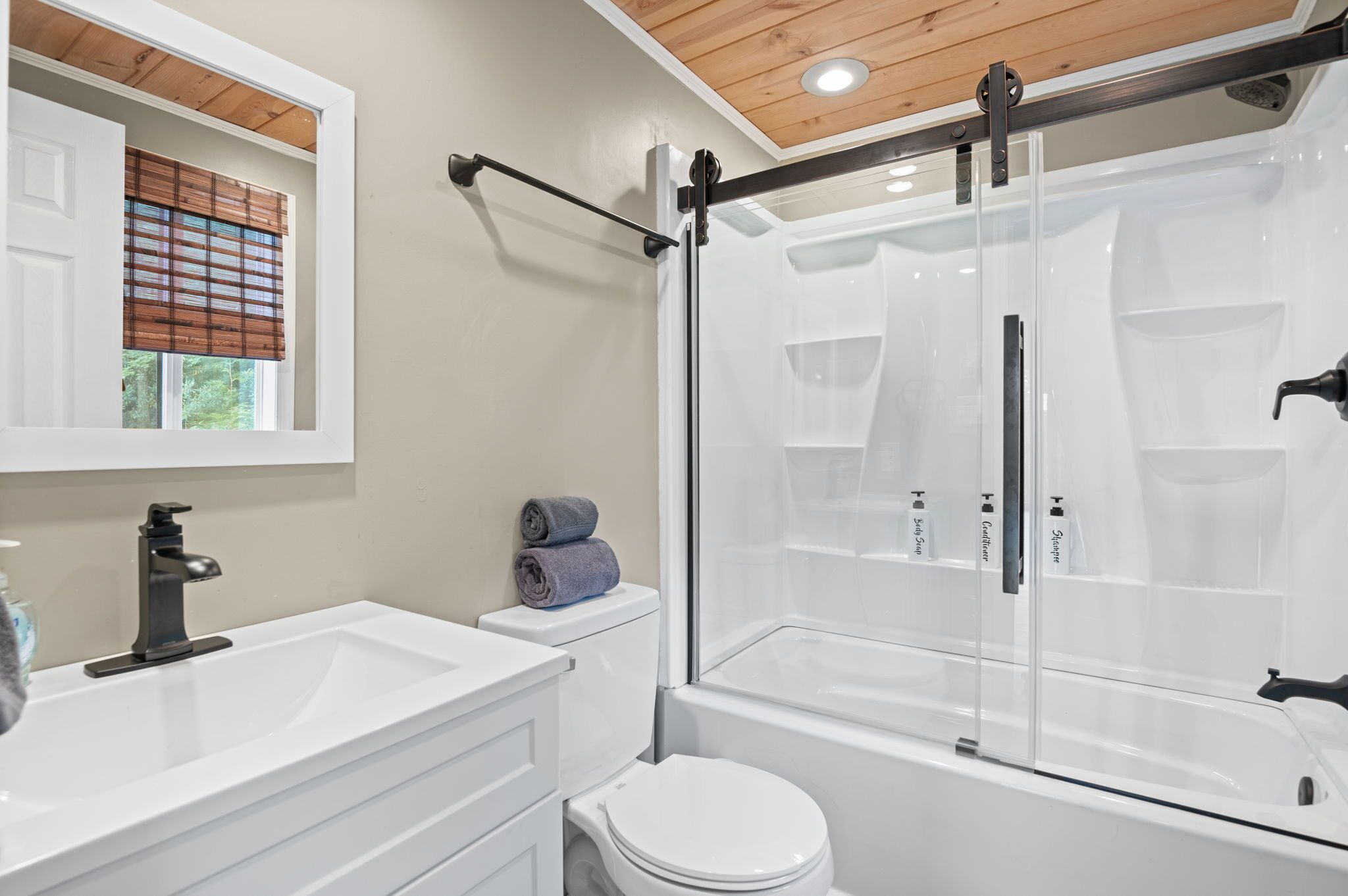A modern bathroom with a glass-enclosed shower, white fixtures, and a window with blinds.