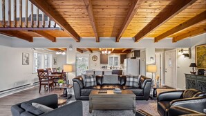 A spacious living area with a high ceiling, wooden beams, a leather sofa, a dining table, and a kitchen in the background. - Walk to Town-Lake Views-6 Decks-Pool Table-FirePit: The Lookout (Lake Harmony)