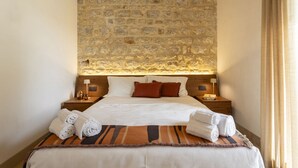 A hotel room with a stone wall, a large bed with white linens, brown pillows, and two bedside tables with lamps.