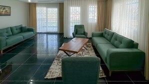 Un salón amplio con un conjunto de sofá verde, una mesa de centro de madera y una alfombra estampada.