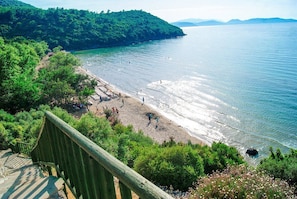 A beach with a wooden staircase leading down to the shore, surrounded by lush greenery and a clear view of the sea. - Villa Begonvil (Kusadasi)