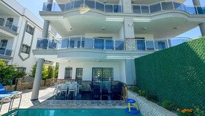 Un edificio residencial de varios pisos con piscina, mobiliario exterior y un seto verde.