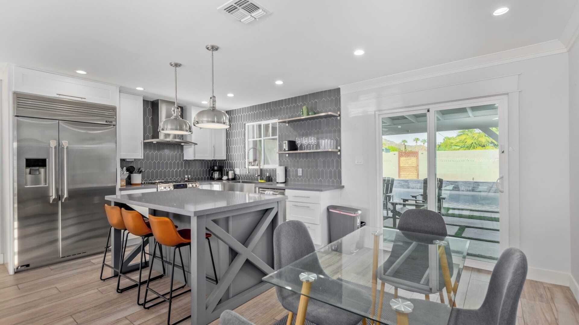 A modern kitchen with a central island, bar stools, and a glass dining table.