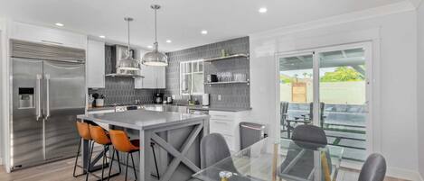 A modern kitchen with a central island, bar stools, and a glass dining table.