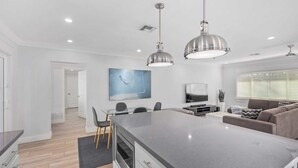 Una cocina moderna con una isla central, comedor con sillas, un sofá y un televisor.