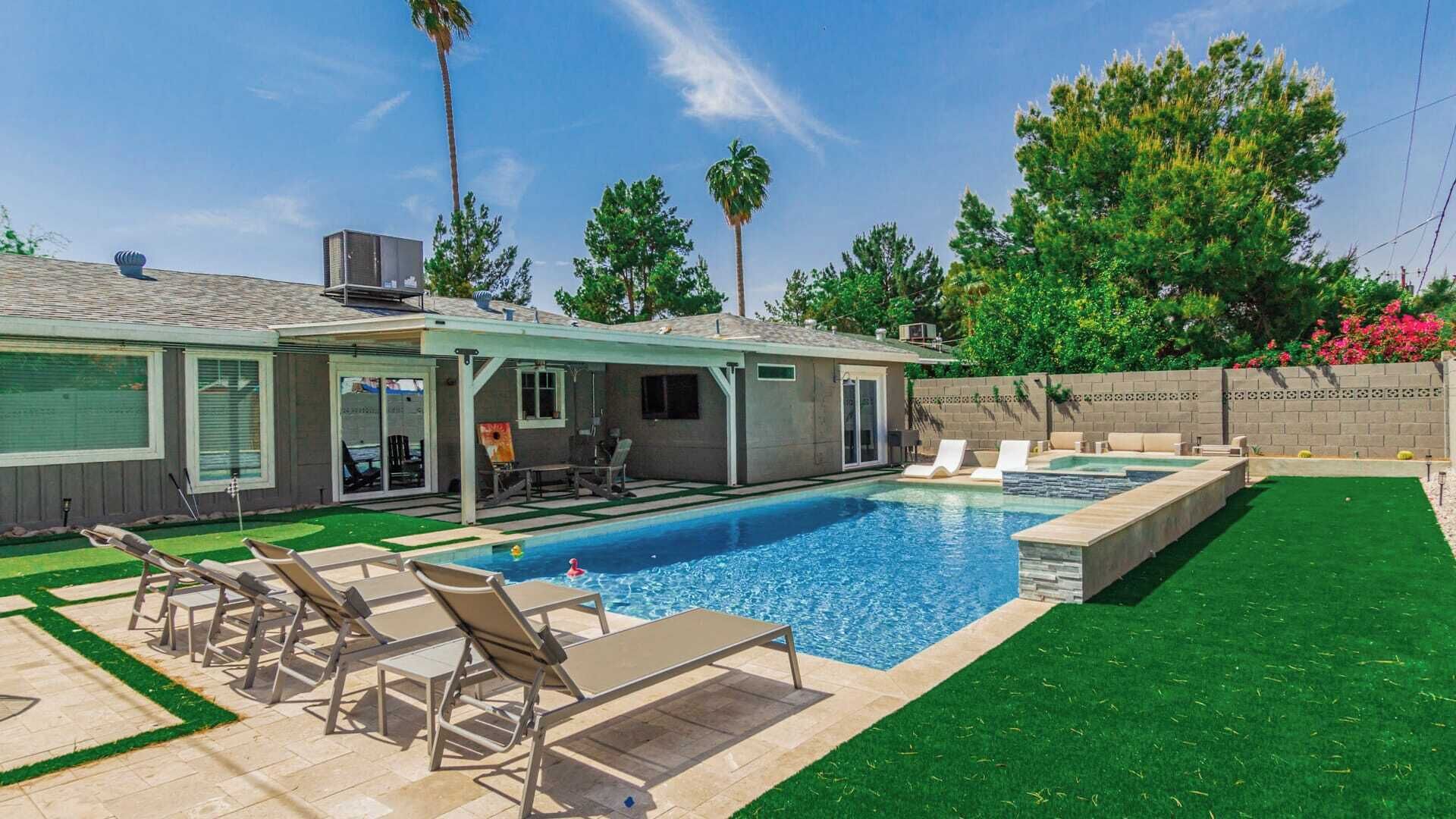 A backyard with a swimming pool, lounge chairs, and a patio area.