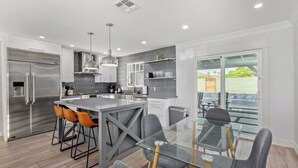 Una cocina moderna con un refrigerador de acero inoxidable, taburetes de bar, una mesa de comedor de vidrio y vistas al exterior.
