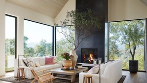 A modern living room with a fireplace, large windows, and a view of the outdoors. - Luxury Villa | Pool, Hot Tub & Views | Glen Ellen | 4BR | Sleeps 8 (Glen Ellen)