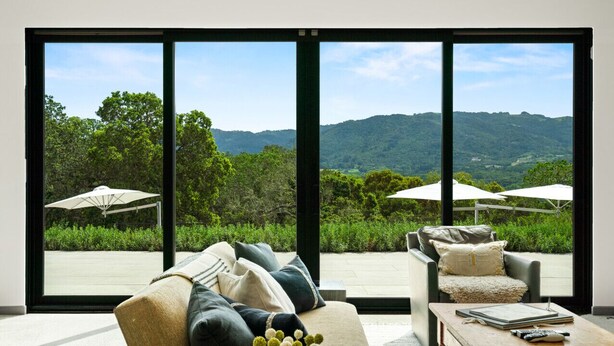 A modern living room with a large sliding glass door leading to a balcony with outdoor umbrellas. - Luxury Villa | Pool, Hot Tub & Views | Glen Ellen | 4BR | Sleeps 8 (Glen Ellen)