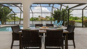 An outdoor dining area with a pool view, wicker chairs, and a table set for four. - For your family, perfect location and amenities that leave nothing to be desired (Cape Coral)