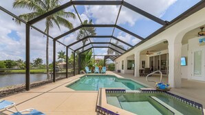 A covered outdoor pool area with lounge chairs, a hot tub, and a view of a lake. - For your family, perfect location and amenities that leave nothing to be desired (Cape Coral)