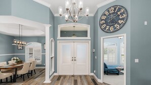 A hallway with a chandelier, a large wall clock, and a double door leading to another room. - For your family, perfect location and amenities that leave nothing to be desired (Cape Coral)