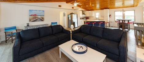 A modern living room with dark sofas, a white coffee table, and a wooden ceiling.