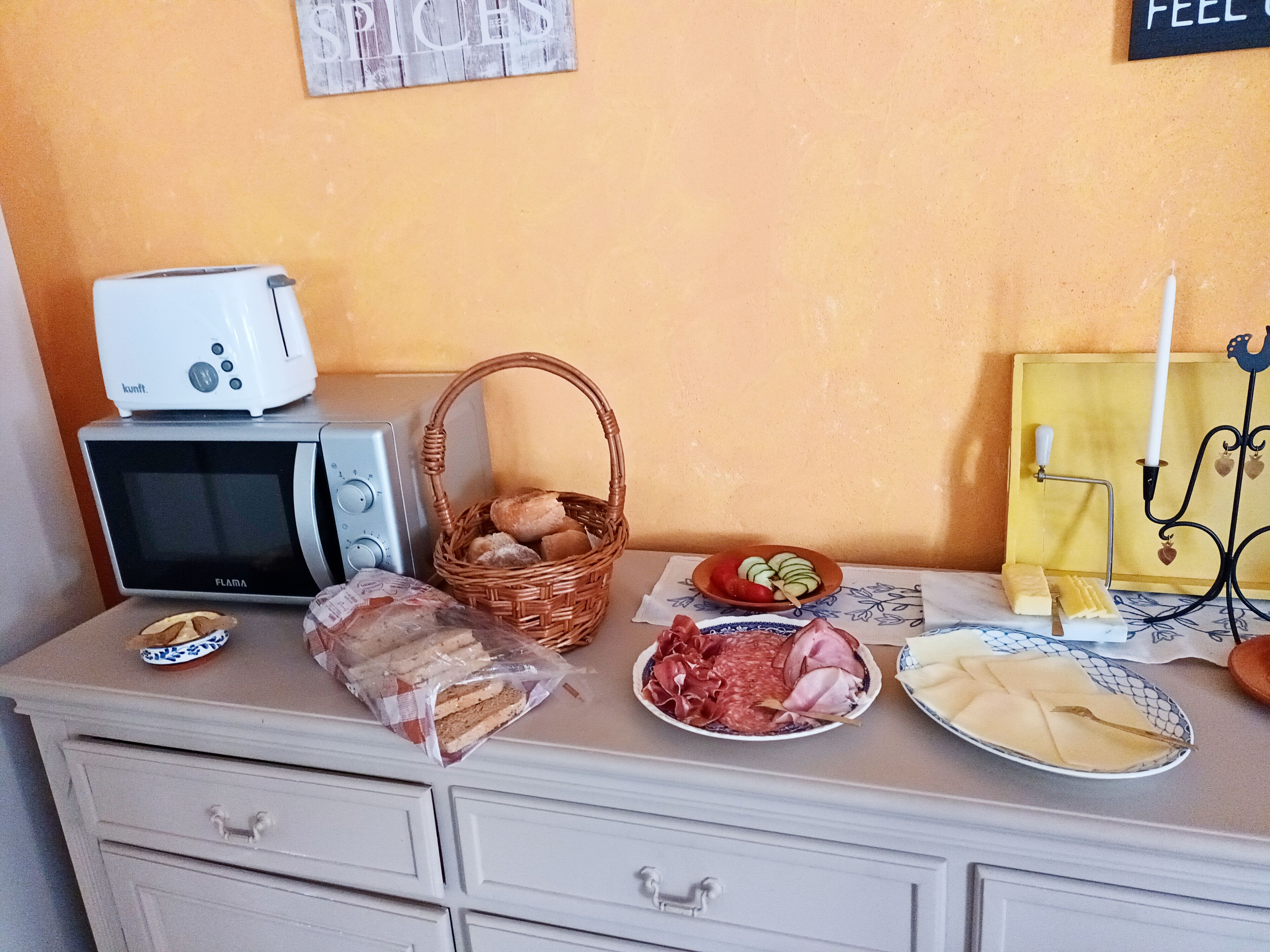 A kitchen counter with a toaster, microwave, basket of bread, and various food items.