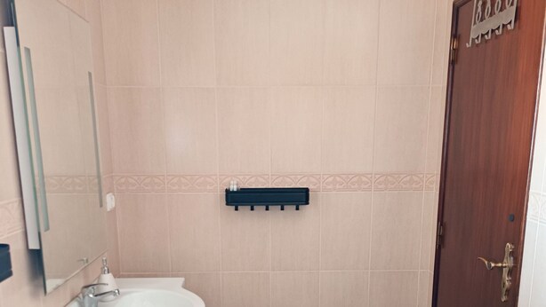 A bathroom with beige tiles, a white sink, a dark cabinet, a wooden door, and a patterned rug. - B&B Quinta da Romãzeira (Silves)