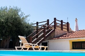 A pool area with a wooden staircase leading to a stone building, a white chair, and a clear blue sky. - B&B Quinta da Romãzeira (Silves)