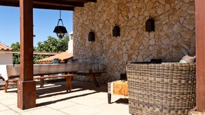 An outdoor patio with a stone wall, wooden furniture, and hanging lanterns. - B&B Quinta da Romãzeira (Silves)