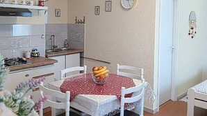 Une cuisine de taille réduite, équipée d’une cuisinière à gaz, de meubles blancs et d’une horloge à cadre rouge accrochée au mur.