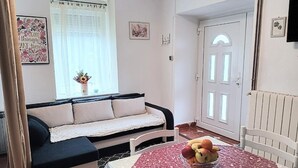 Une pièce chaleureuse avec un canapé, une table à manger sur laquelle se trouve un panier de fruits, une fenêtre avec des rideaux et une porte.