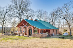A rustic cabin with a green roof, stone foundation, and a porch area. - Expansive Mountain Home Rental w/ Yard & Fire Pit! (Mountain Home)