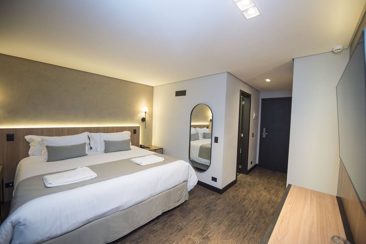 A hotel room with a large bed, a bedside table, a mirror, and a door.