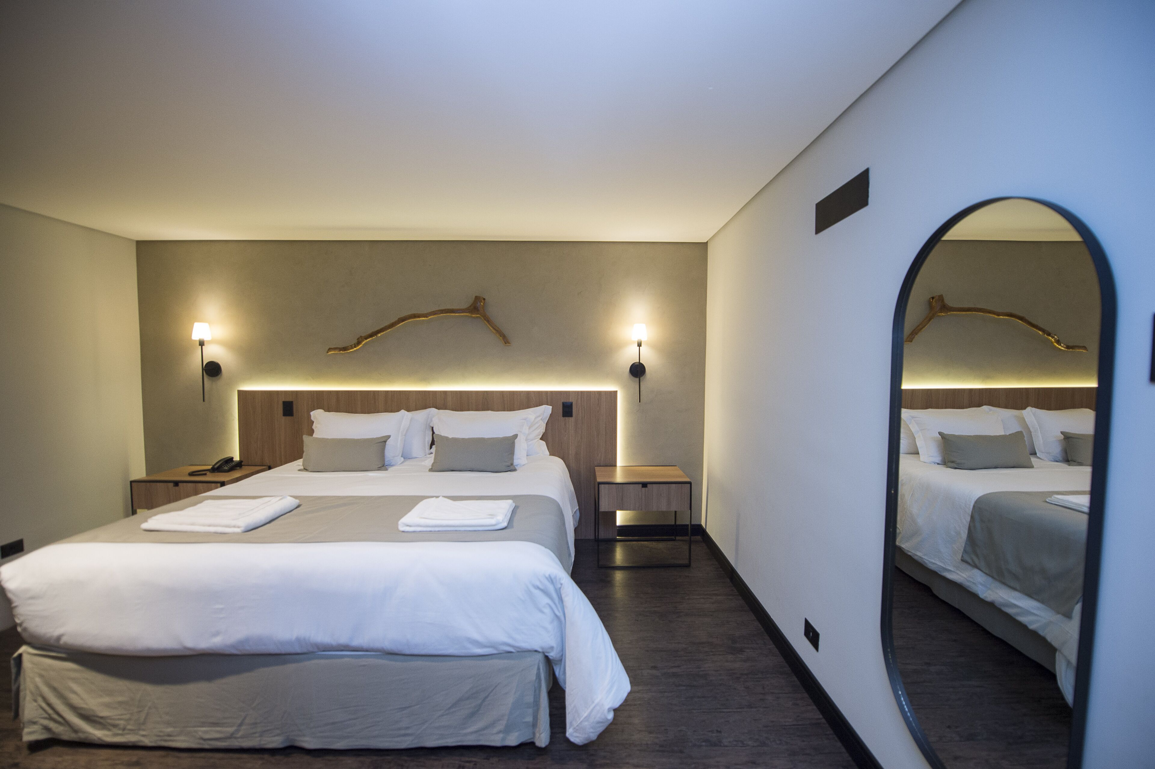 A hotel room with a large bed, bedside tables, a mirror, and wall-mounted lamps.
