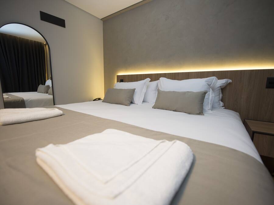 Une chambre d’hôtel moderne dotée d’un grand lit, d’une table de chevet, d’un miroir et d’une tête de lit avec un éclairage intégré.