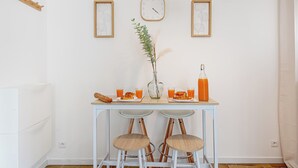 Zona pranzo con tavolo apparecchiato per due, con orologio, quadro incorniciato e vaso con piante.