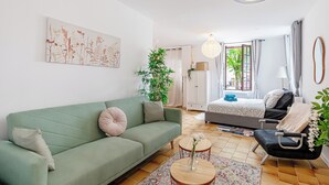 Un soggiorno moderno con un divano verde, un tavolino rotondo e una poltrona nera. Si vede un letto sullo sfondo con copripiumino bianco e grigio.