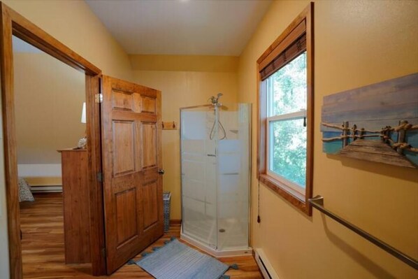 Un pasillo con puerta de madera, cabina de ducha de vidrio y ventana con vistas a árboles.