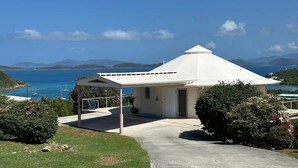 A white building with a conical roof, a covered patio, and a view of the sea and mountains. - The Round House (St Thomas)