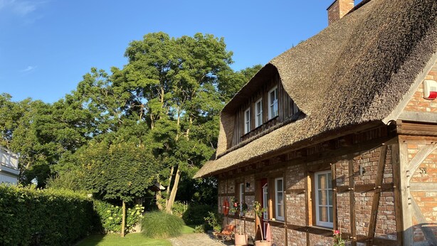 Un bâtiment traditionnel en pierre, avec un toit de chaume, une allée pavée et une voiture garée devant.