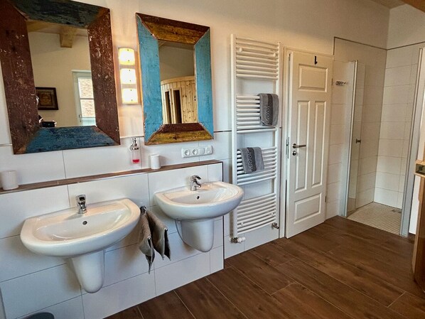 A bathroom with two sinks, a mirror, a towel rack, and a shower area. - Ferienhaus " To Huus ", 6 Pers., 3 Schlafzimmer, Kamin, Sauna, Wlan (Rosenhagen)