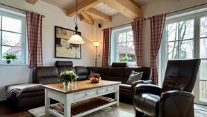 Ein gemütliches Wohnzimmer mit einem Holztisch, Ledersofas und einem großen Fenster mit Vorhängen.