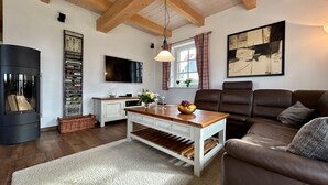 Un salon avec un plafond en bois, une table basse blanche, un canapé marron et un téléviseur fixé au mur.