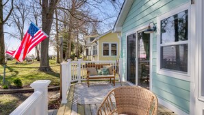 A wooden deck with a wicker chair and a bench, a white fence, and a house with large windows. - Bayfront Maryland Retreat w/ Deck, Near Beaches! (North Beach)