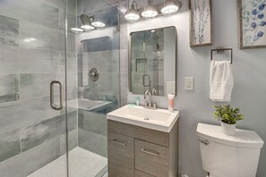 Ein modernes Badezimmer mit Duschkabine aus Glas, Waschbecken mit Spiegel darüber und Toilette mit Blumentopf.