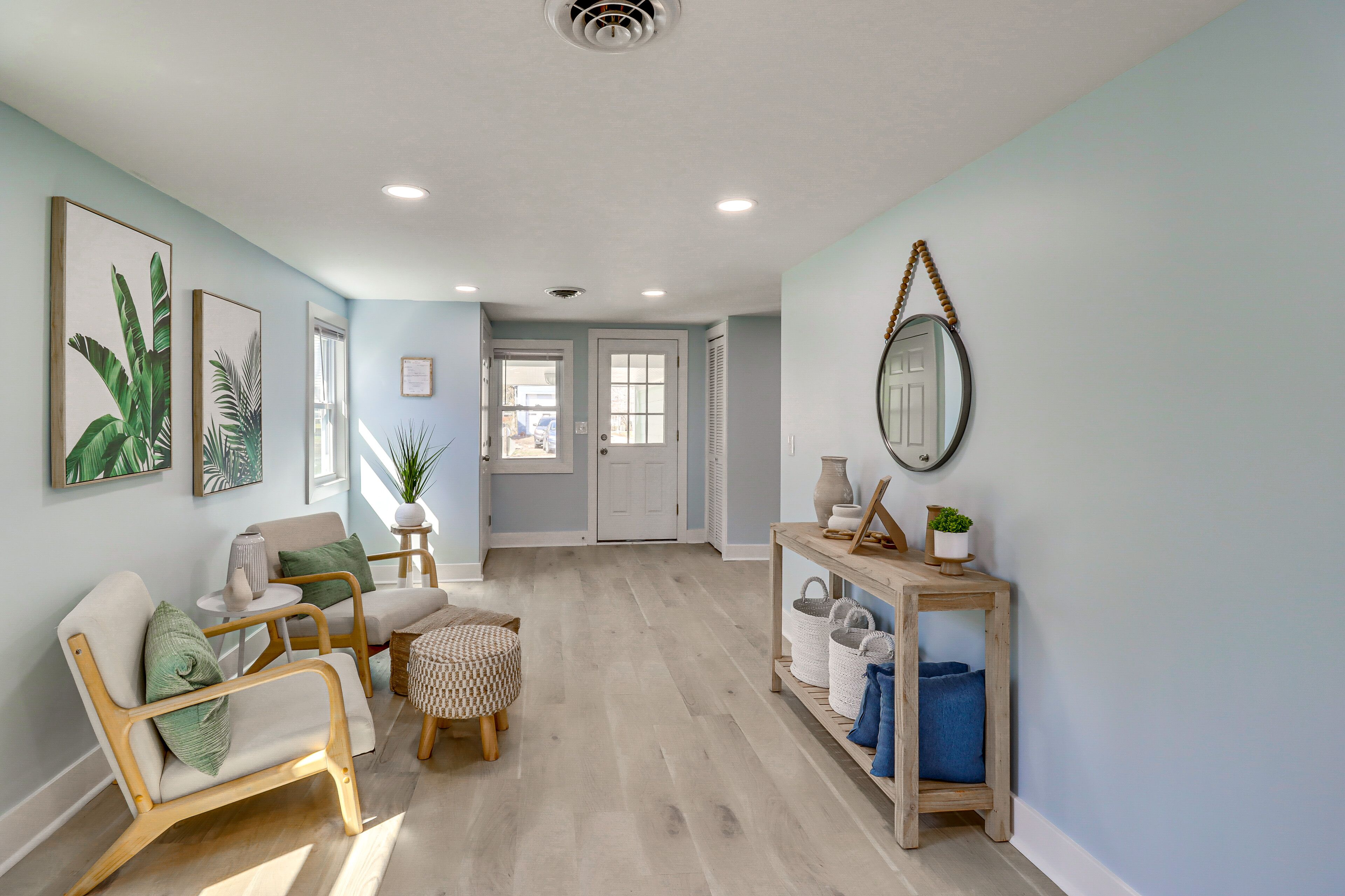 A spacious hallway with a light blue wall, wooden flooring, and a seating area with a chair and ottoman.