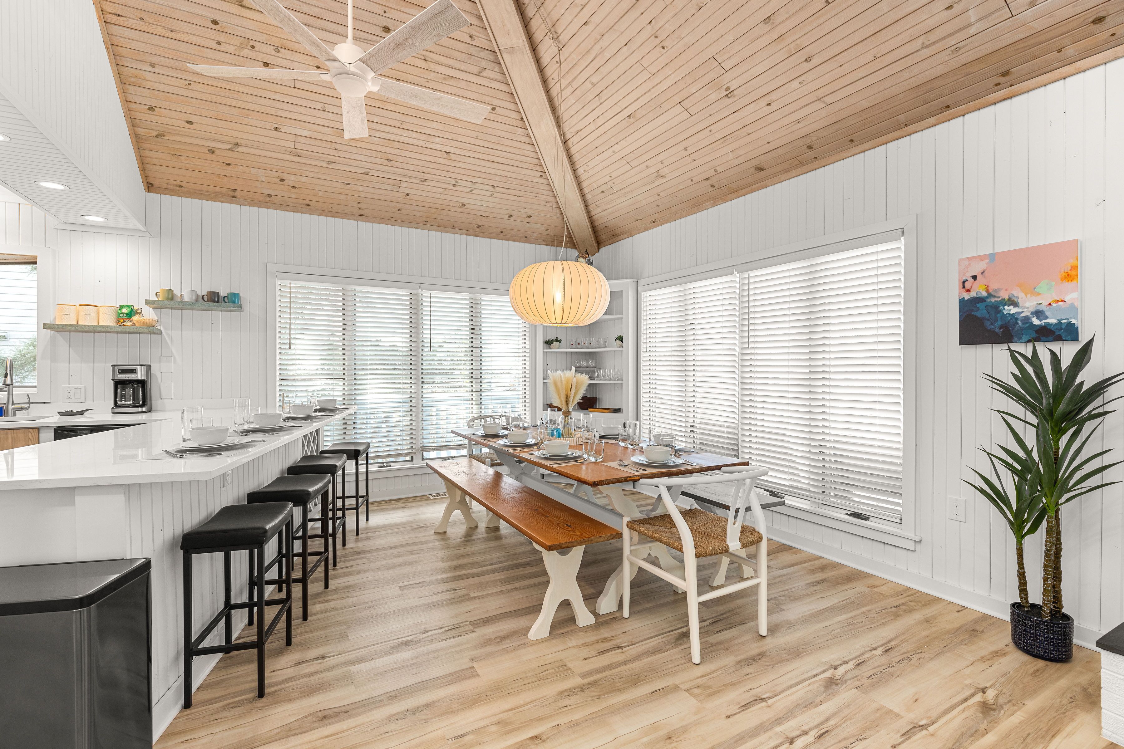 A modern kitchen with a wooden ceiling, white walls, and a central island with bar stools.