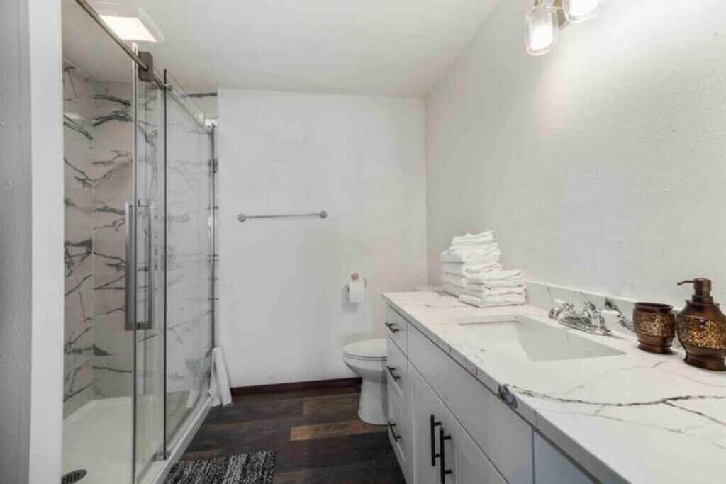 Un baño moderno con cabina de ducha de vidrio, inodoro blanco, lavabo con azulejos de mármol y tocador con espejo.