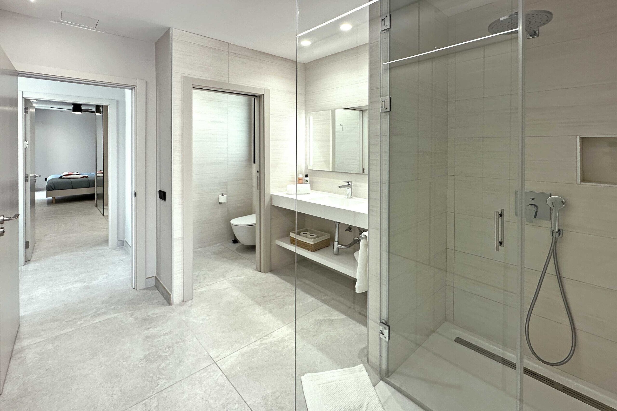 Une salle de bain moderne dotée d’une douche à parois de verre, de toilettes et d’un espace lavabo avec un miroir.