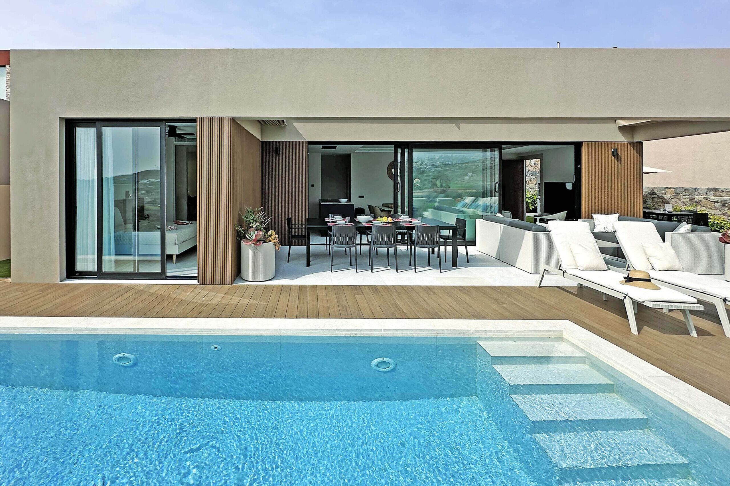 Un área de piscina moderna al aire libre con mobiliario para comer y sillones de descanso.