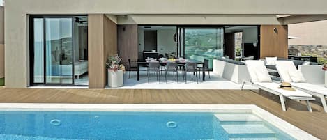 Un área de piscina moderna al aire libre con mobiliario para comer y sillones de descanso.