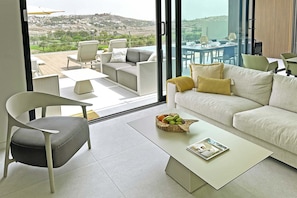 A modern living room with a sofa, a chair, a coffee table with a fruit basket, and a view of the outdoors through large glass doors. - Salobre Los Veroles Golf, Maspalomas (Maspalomas)