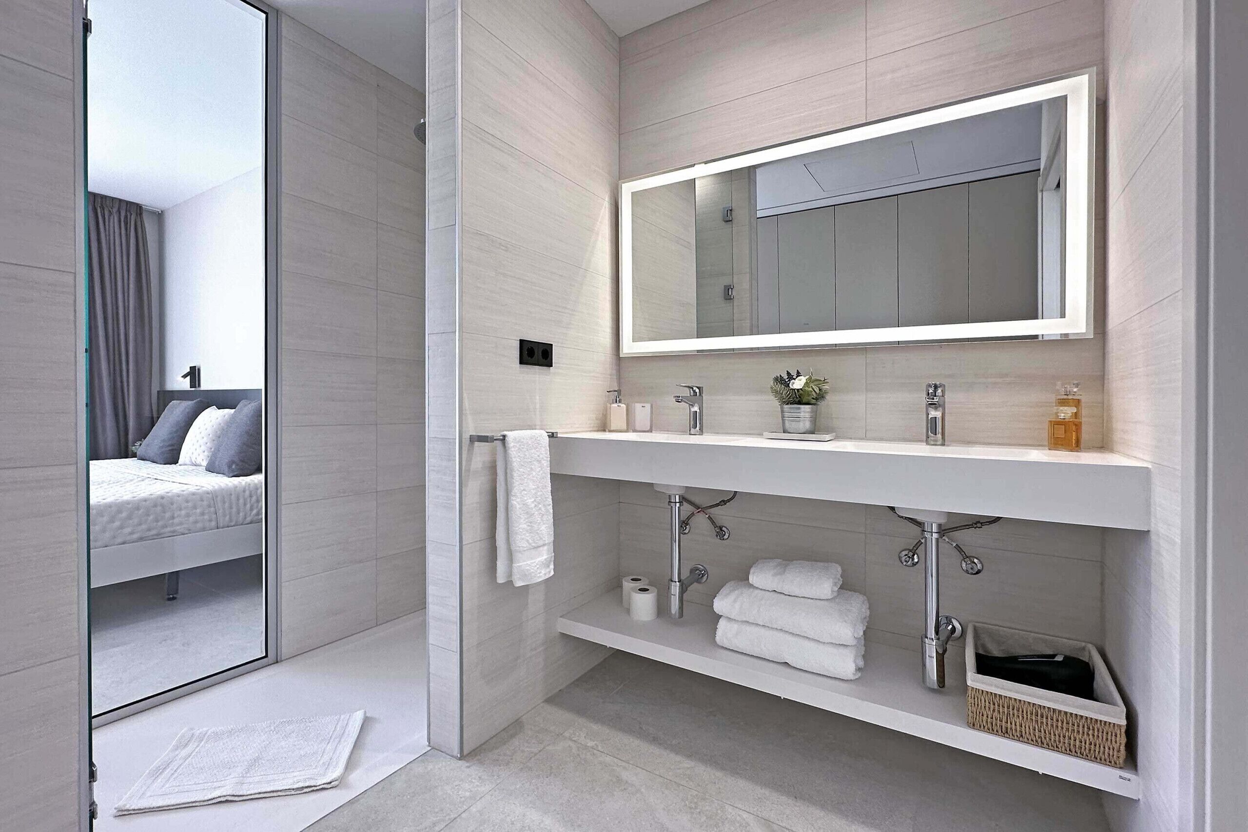 Un baño moderno con un espejo grande, ducha, inodoro y lavamanos.