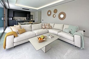 A modern living room with a sectional sofa, a coffee table with fruit, and a kitchen in the background. - Salobre Los Veroles Golf, Maspalomas (Maspalomas)